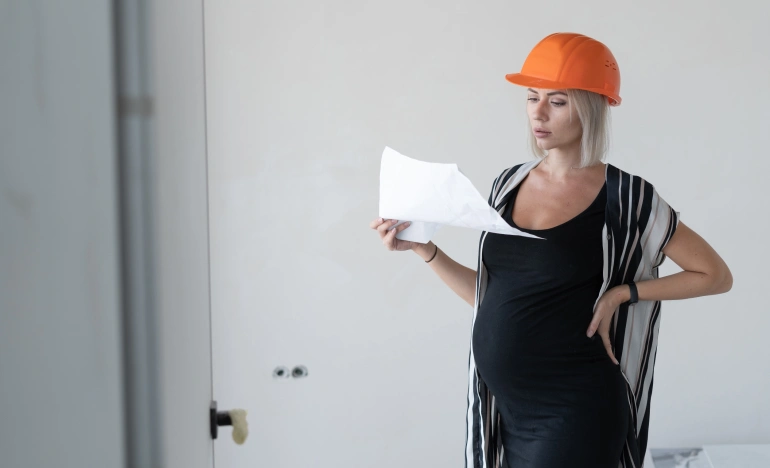 Беременная женщина в строительной каске изучает документ
