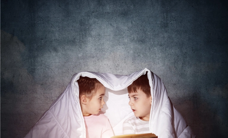 Мальчик и девочка под одеялом читают книгу