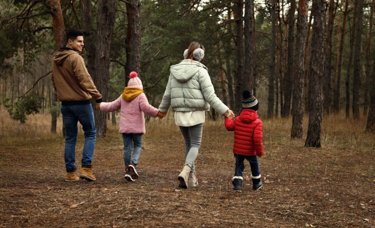 Мужчина, женщина и двое детей идут по лесу взявшись за руки