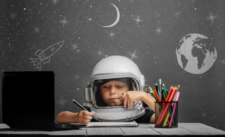 Мальчик в космическом скафандре рисует цветными карандашами