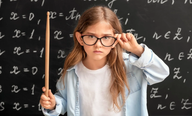 Девочка в очках и указкой стоит у школьной доски 