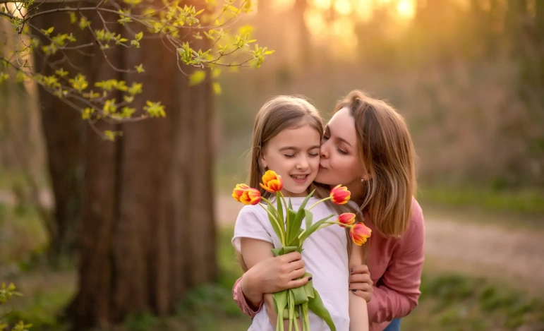 Мать обнимает дочку с цветами в руках